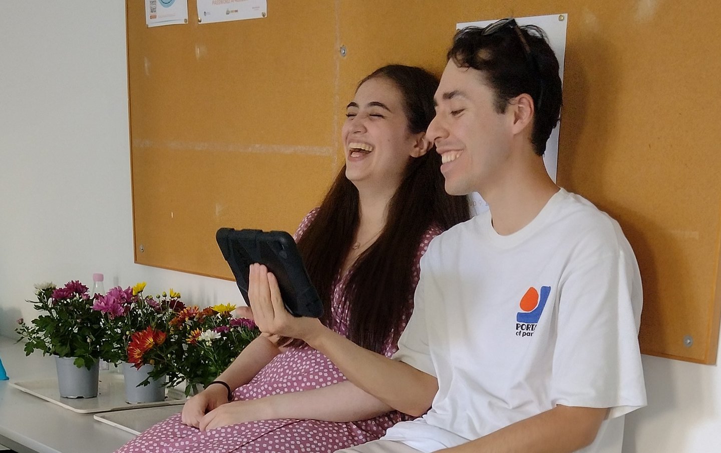 Two oniste buddies sitting next to each other and zooming with an online participant via a tablet